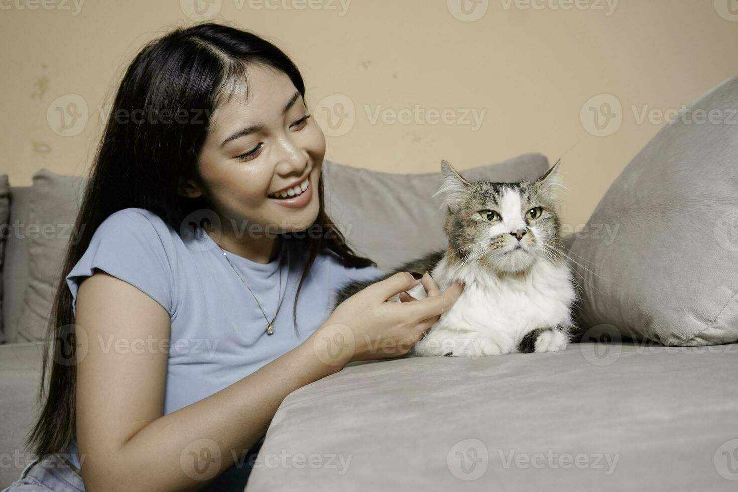 bonito asiático mujer abrazo un gato y sentar en sofá con contento emoción. adorable Doméstico mascota concepto. foto