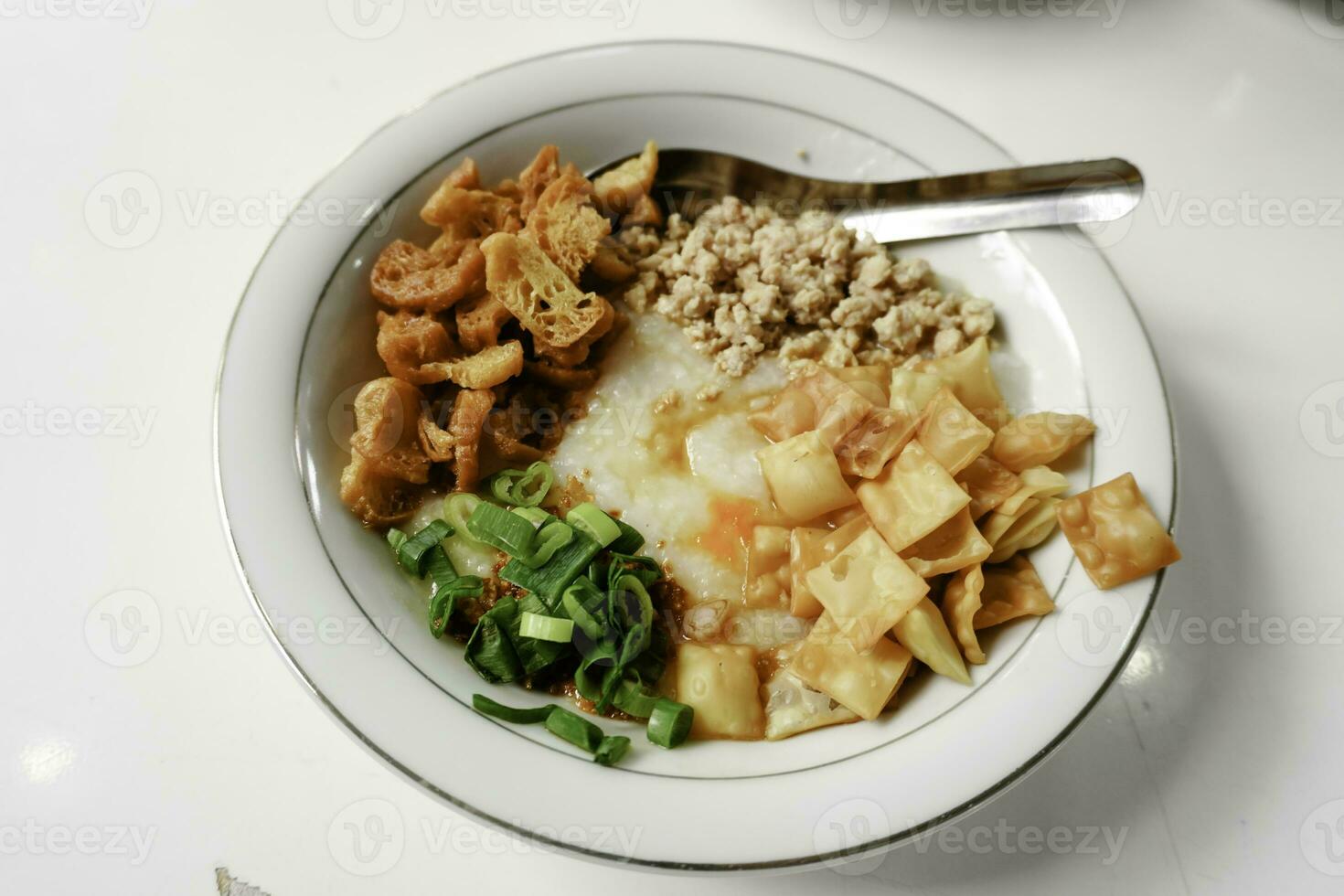 Bubur ayam or Chicken Porridge, Indonesian traditional food consist of white rice porridge, shredded chicken, cakwe, crackers, and leek. Selective focus. photo