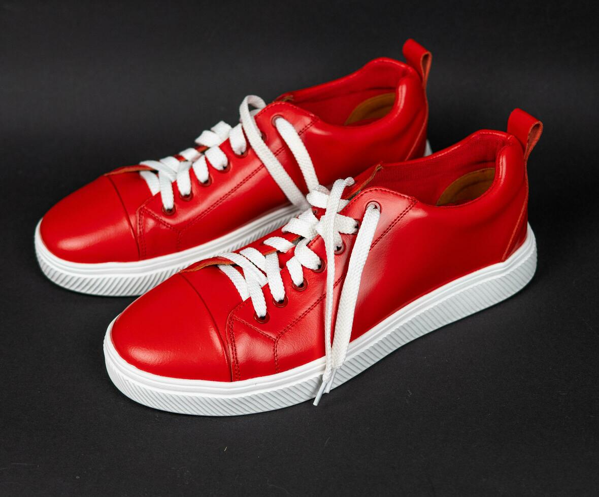 Red leather sneakers with white soles on a black background. new photo