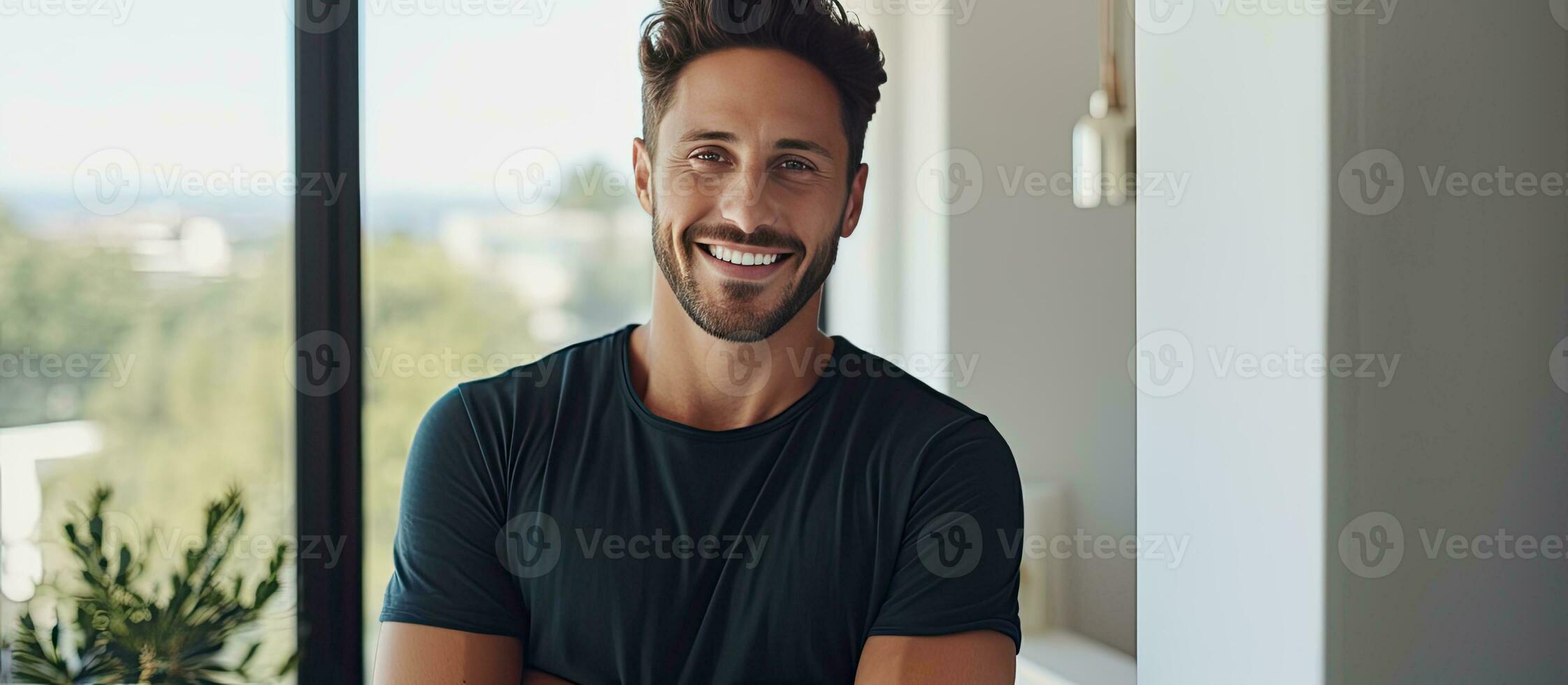 Portrait of a joyful young man holding tablet and smiling at camera by a window photo