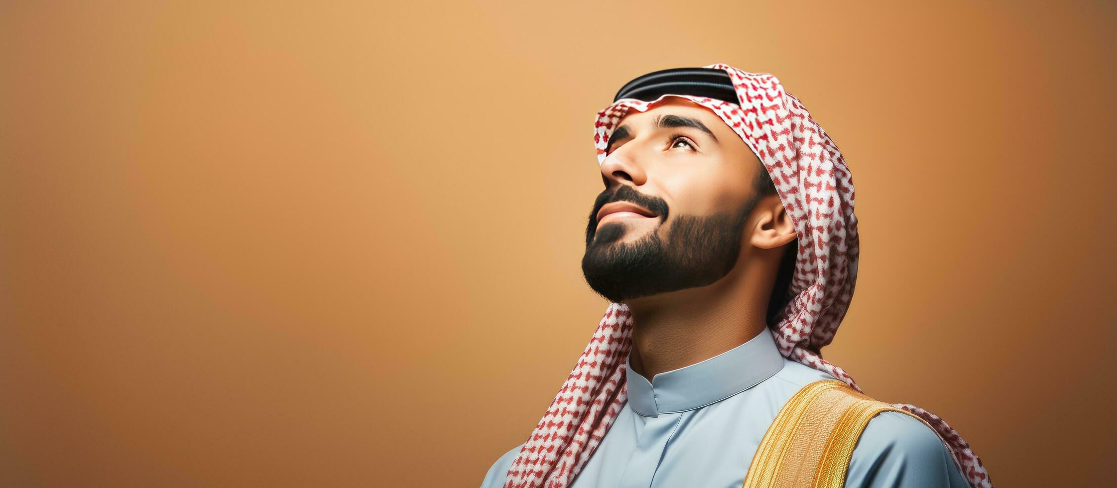 Thoughtful young Arab man daydreaming and looking up against a blank wall photo