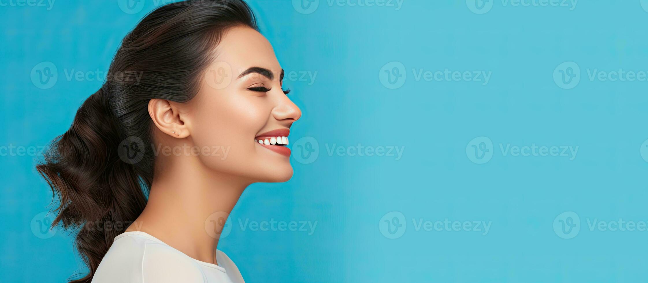 Attractive girl smiling in profile portrait with blue background and copy space photo