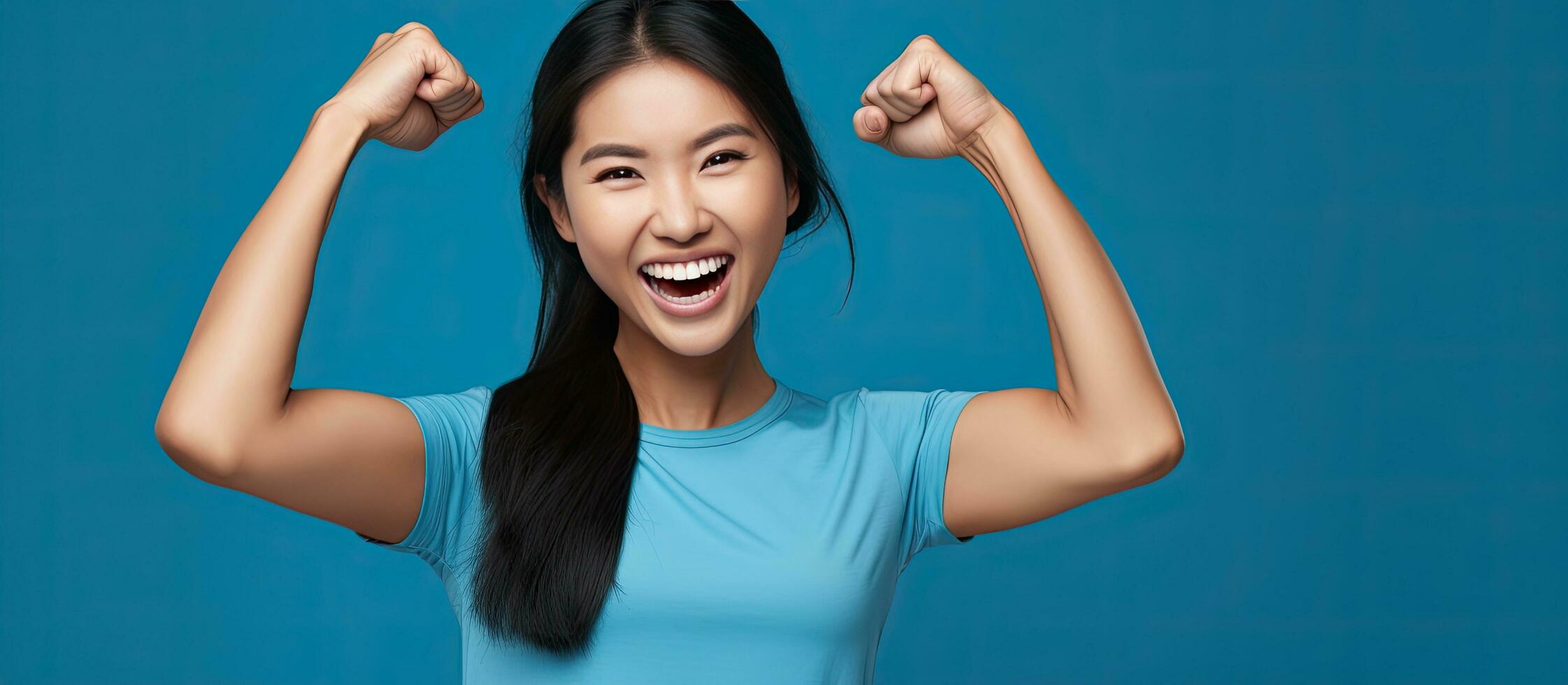 An enthusiastic Asian woman proudly lifting her arms showing off her muscles wearing a blue shirt and smiling photo