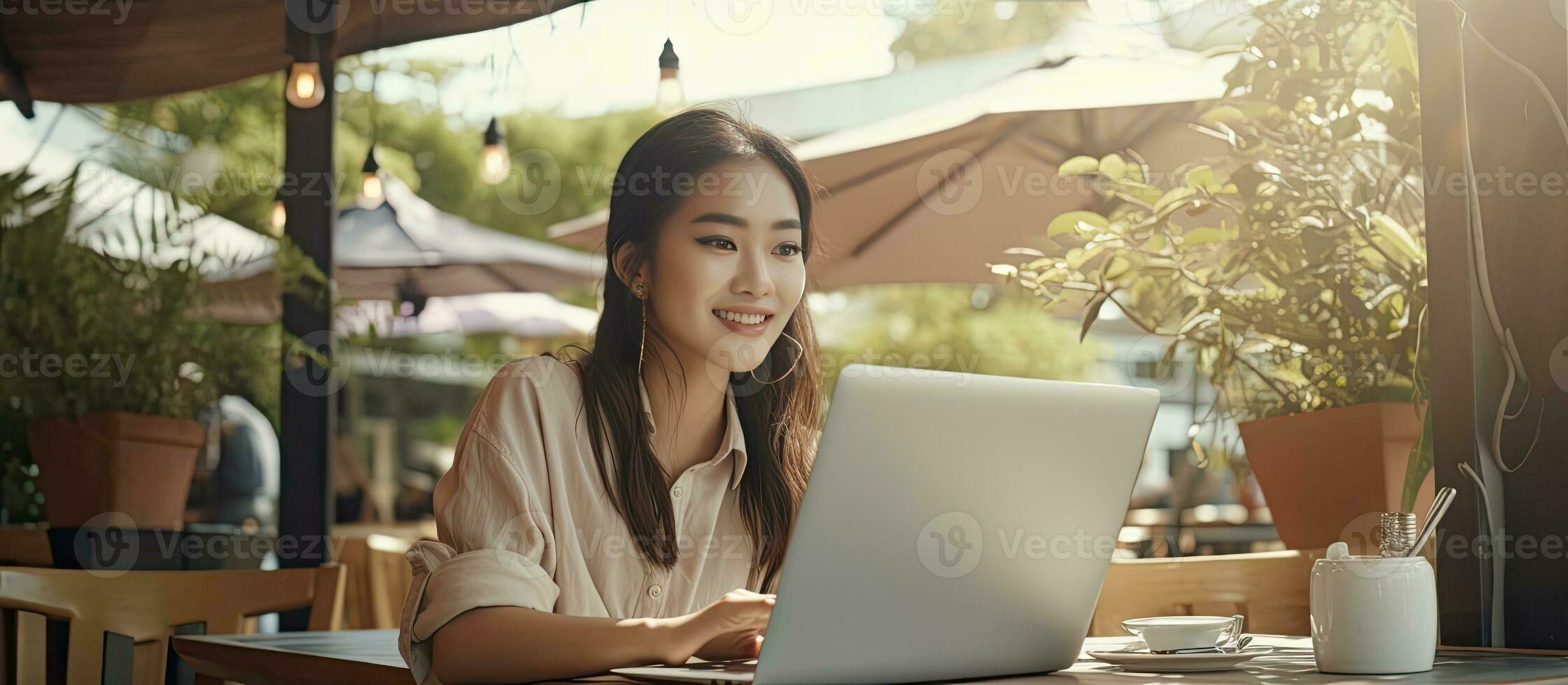 Young Asian woman with laptop at outdoor cafe studying and smiling photo