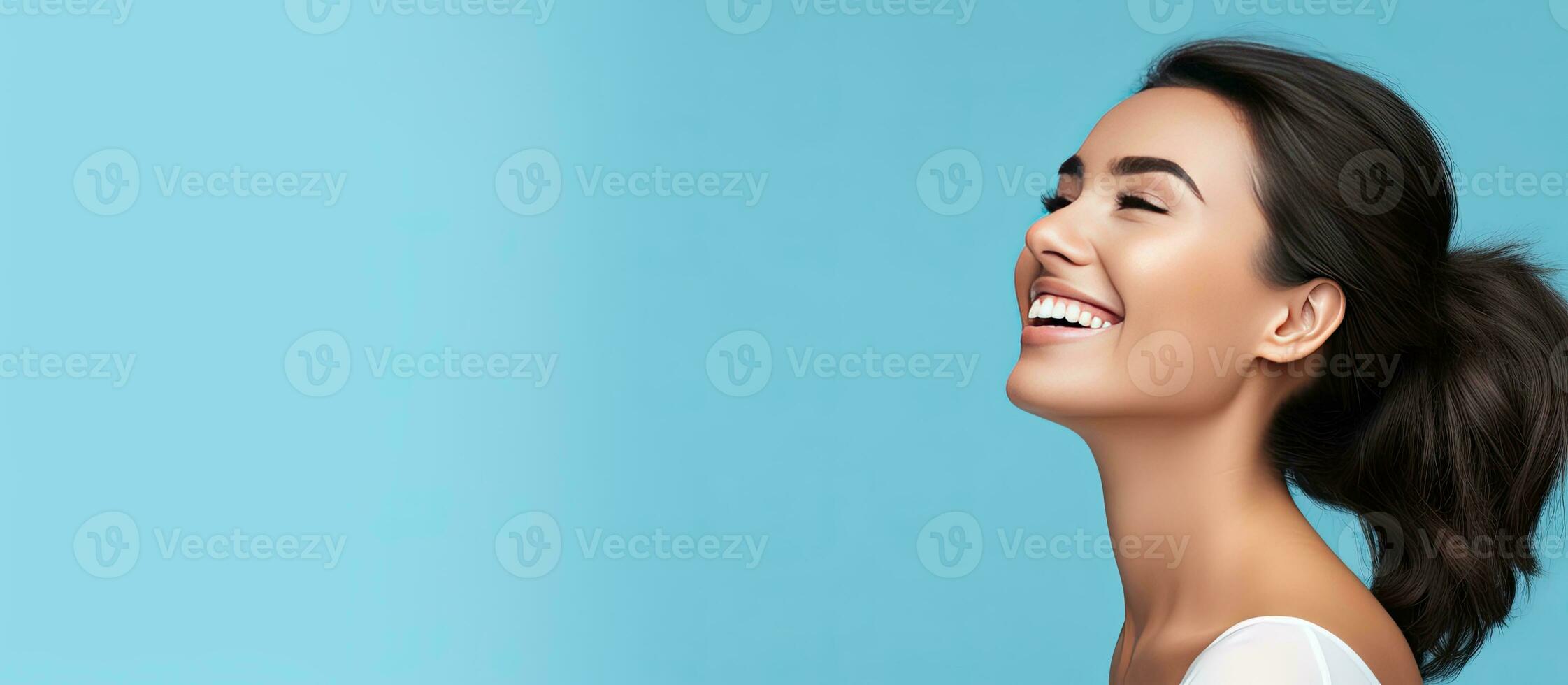 Attractive girl smiling in profile portrait with blue background and copy space photo