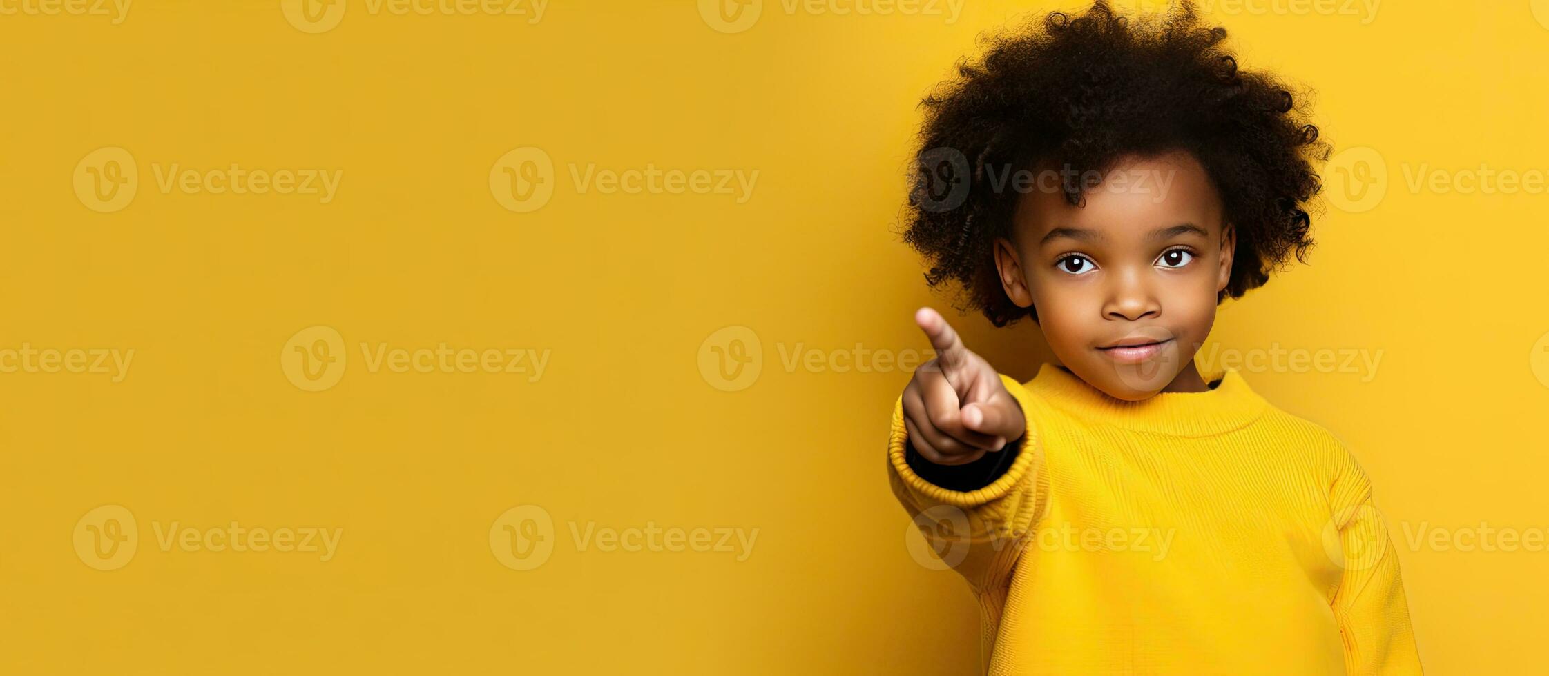 A black girl student is pointing fingers at copy space over a yellow background photo