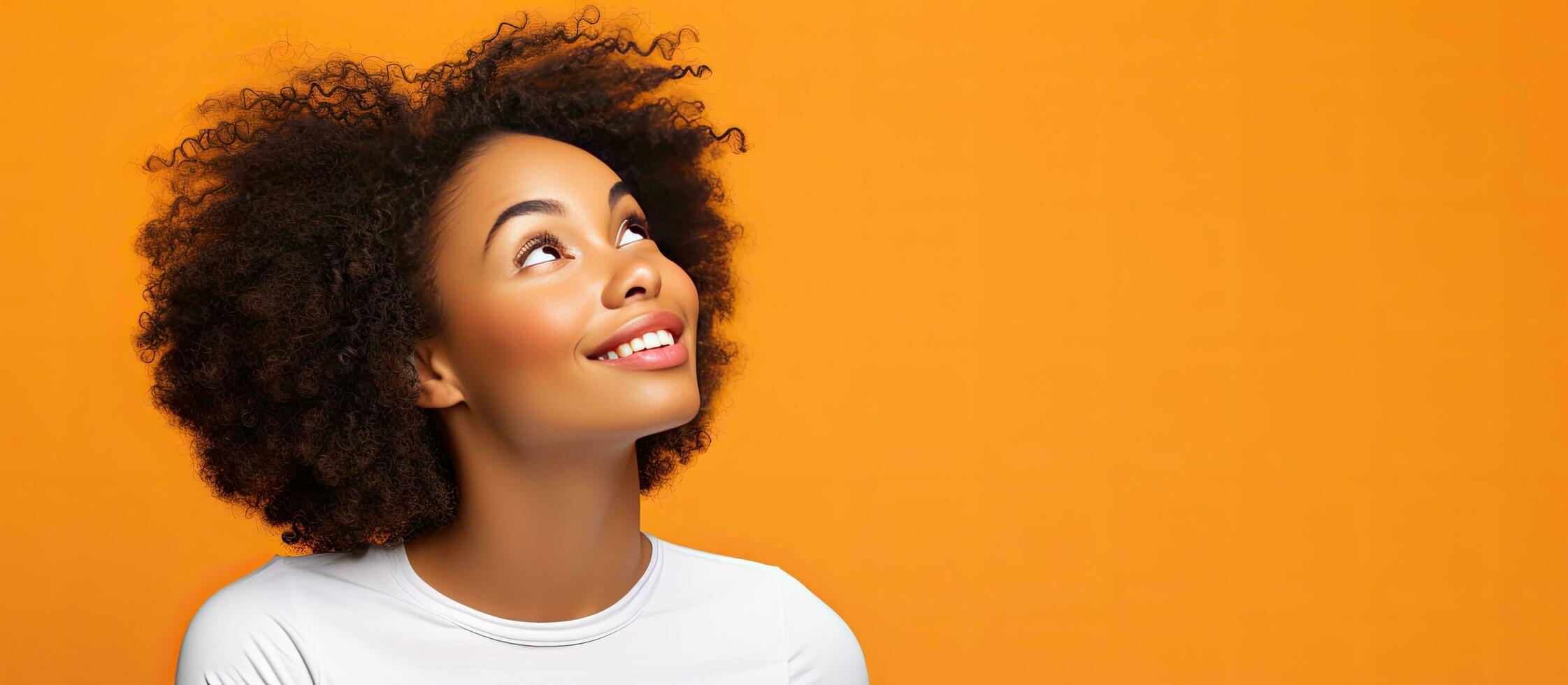A thoughtful young black woman in a white t shirt gazes upward in a studio isolated on an orange background contemplating with space for advertising and o photo