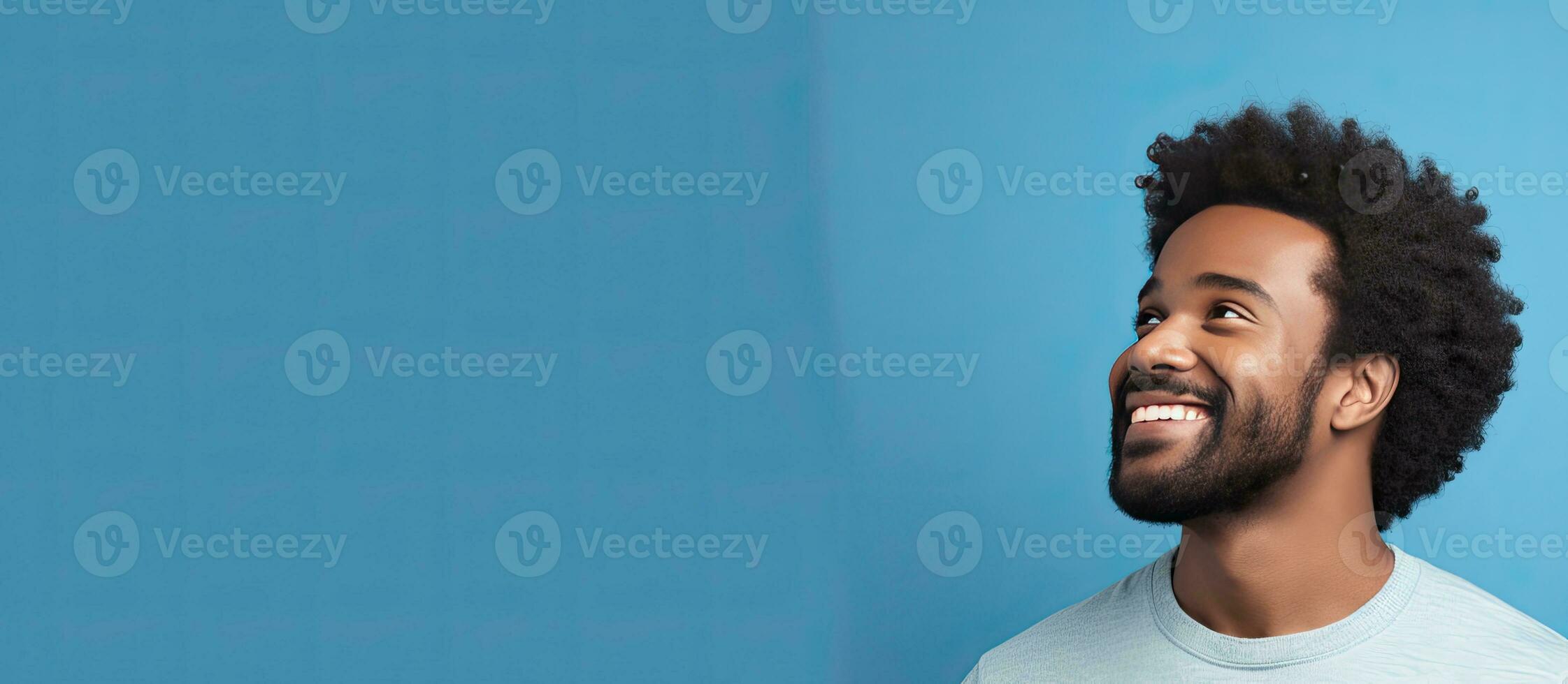 Side view of young African American man smiling and looking aside isolated on blue background with copy space photo