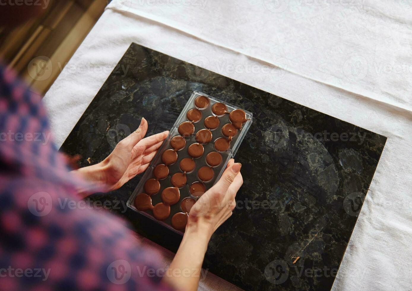 Close-up of female hands holding chocolate molds full of liquid heated chocolate mass. Preparing chocolates for celebrating World Chocolate Day photo