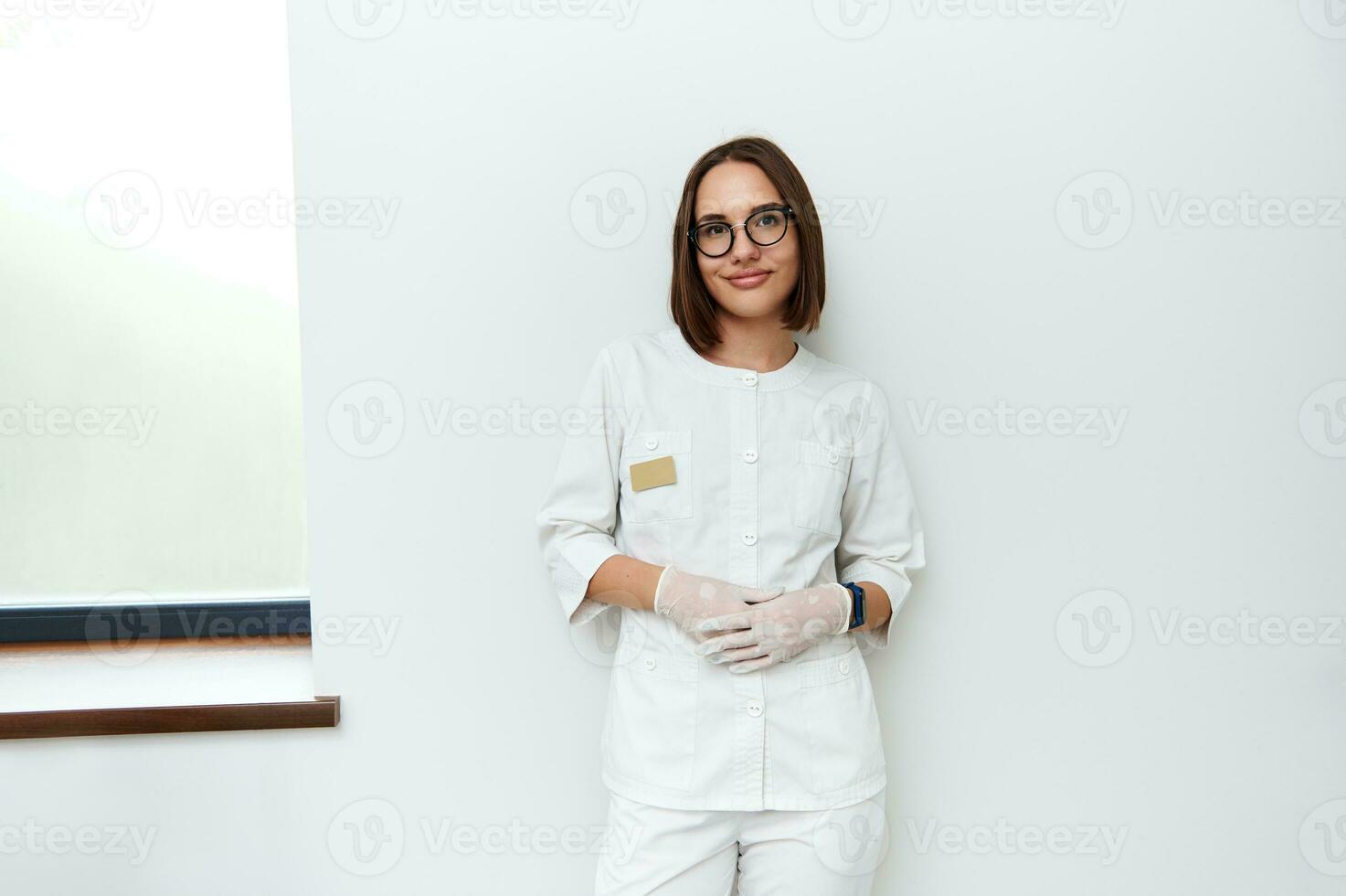 confidente retrato de bonito joven hembra médico propensión en contra blanco pared en médico clínica foto