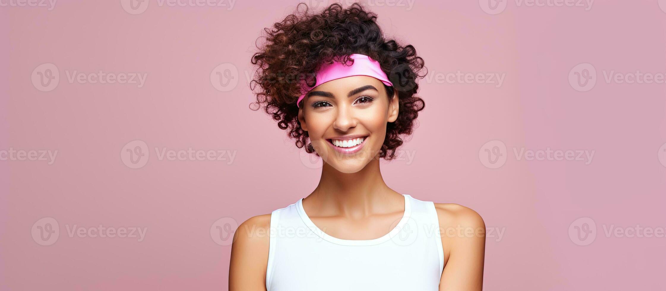 Sporting concept Joyful woman with pink headband curly hair and vibrant top poses on white background leaving room for text photo