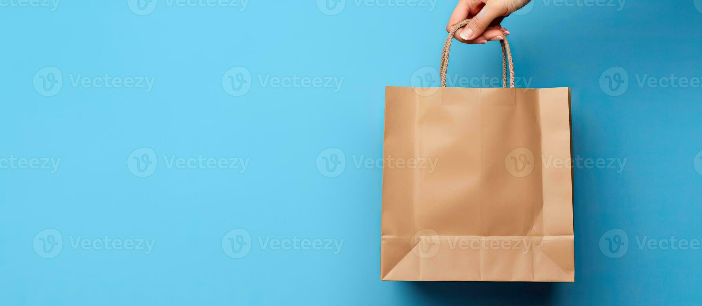Female hand holding brown paper bag with food products isolated on blue wall background Delivery service concept Mock up for advertising photo