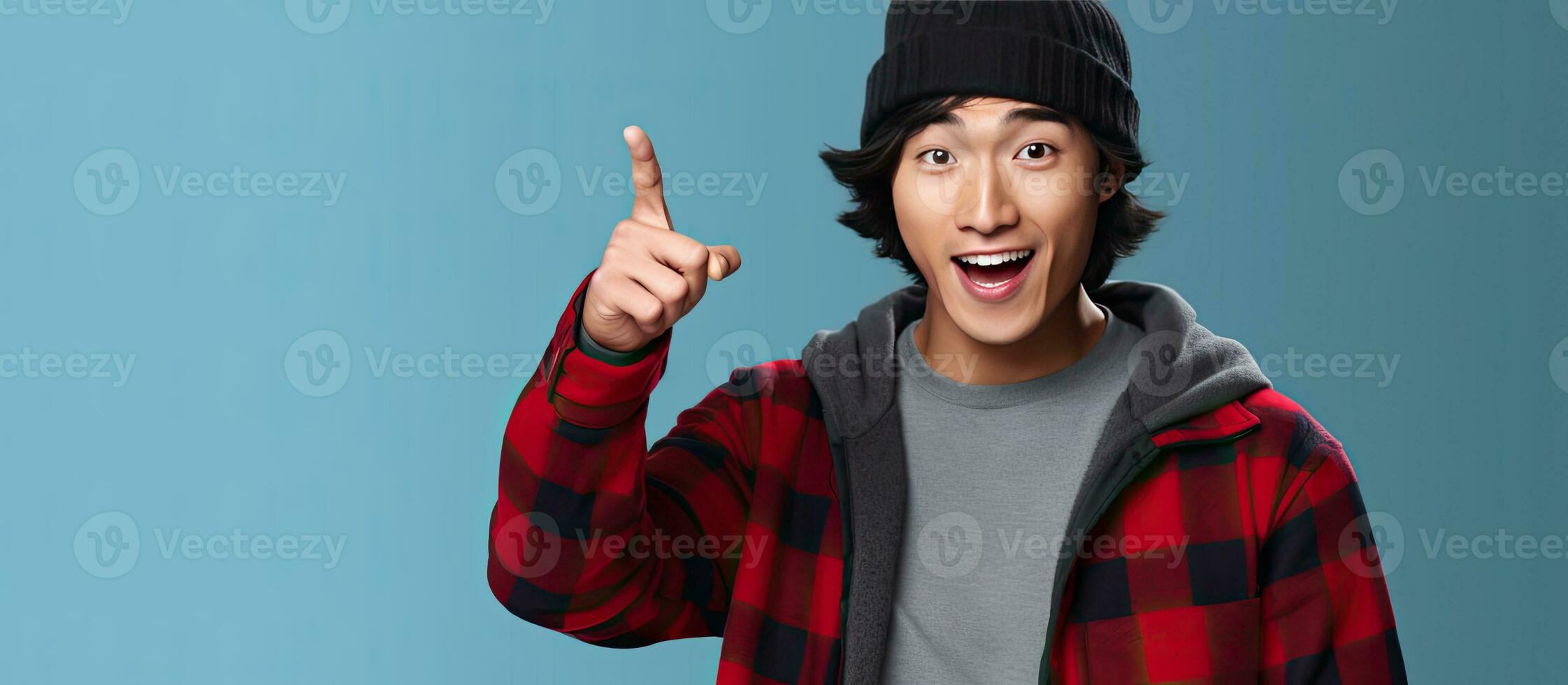 Excited Asian man with beanie hat points at blank mobile phone against blue background photo