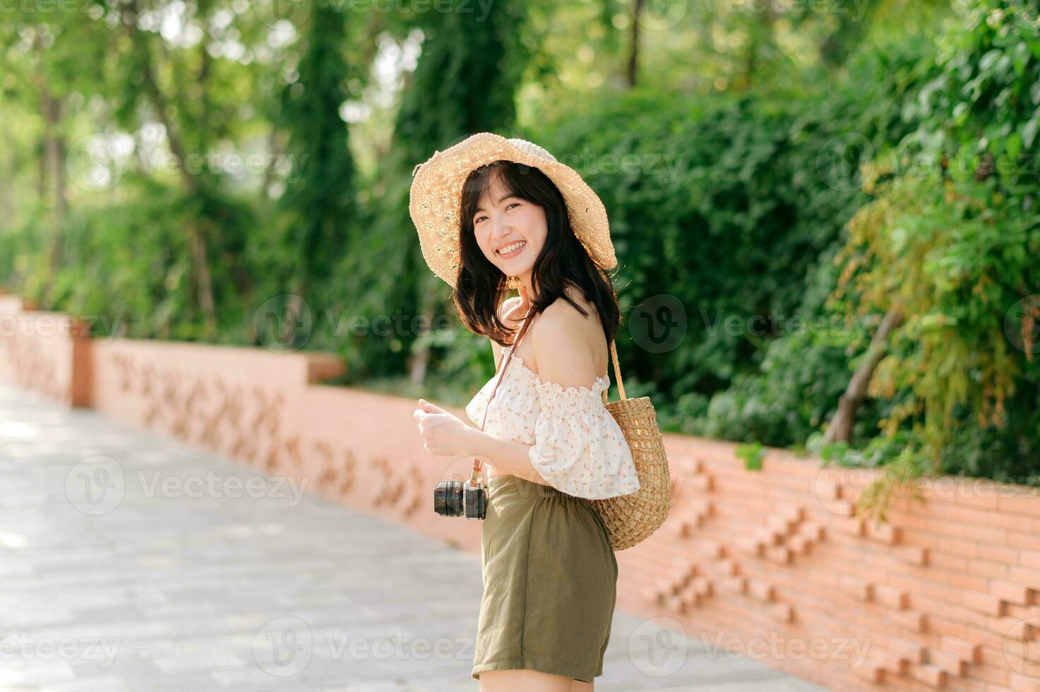 Portrait of asian young woman traveler with weaving hat and basket and a camera on green public park nature background. Journey trip lifestyle, world travel explorer or Asia summer tourism concept. photo