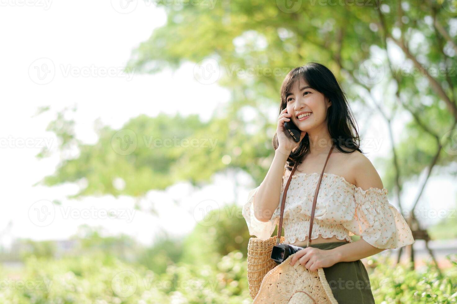 Portrait of asian young woman traveler with weaving hat, basket, mobile phone and camera on green public park background. Journey trip lifestyle, world travel explorer or Asia summer tourism concept. photo