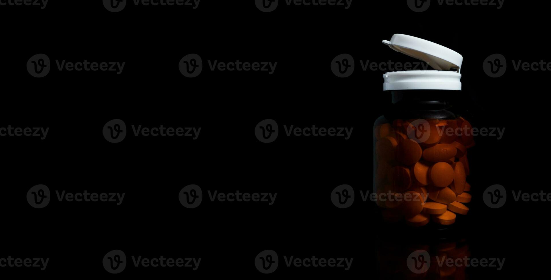 The pills are in the orange medicine bottle on the black background photo