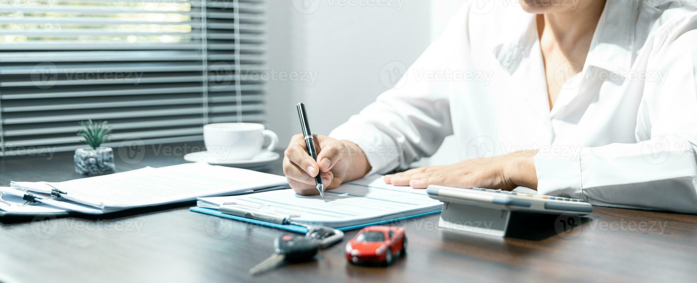 Woman signing car insurance document or lease paper. Writing signature on contract or agreement. Buying or selling new or used vehicle. Car keys on table. Warranty or guarantee. Customer or salesman. photo