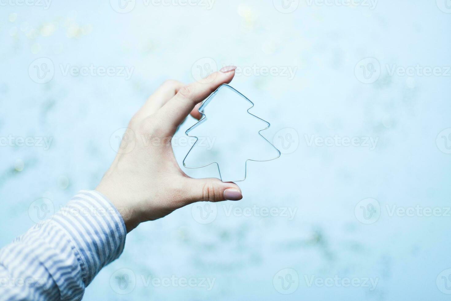 A hand holds a Christmas tree shaped cookie cutter. Bake Christmas cookies photo