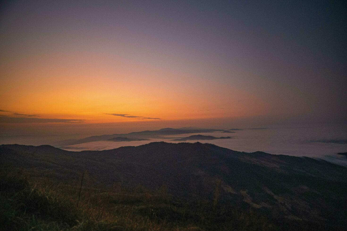 The stunning view from a tourist's standpoint as they go down a hill on a foggy trail with a hill and a background of a golden sky in Phu Langka Forest Park in Phayao, Thailand. photo