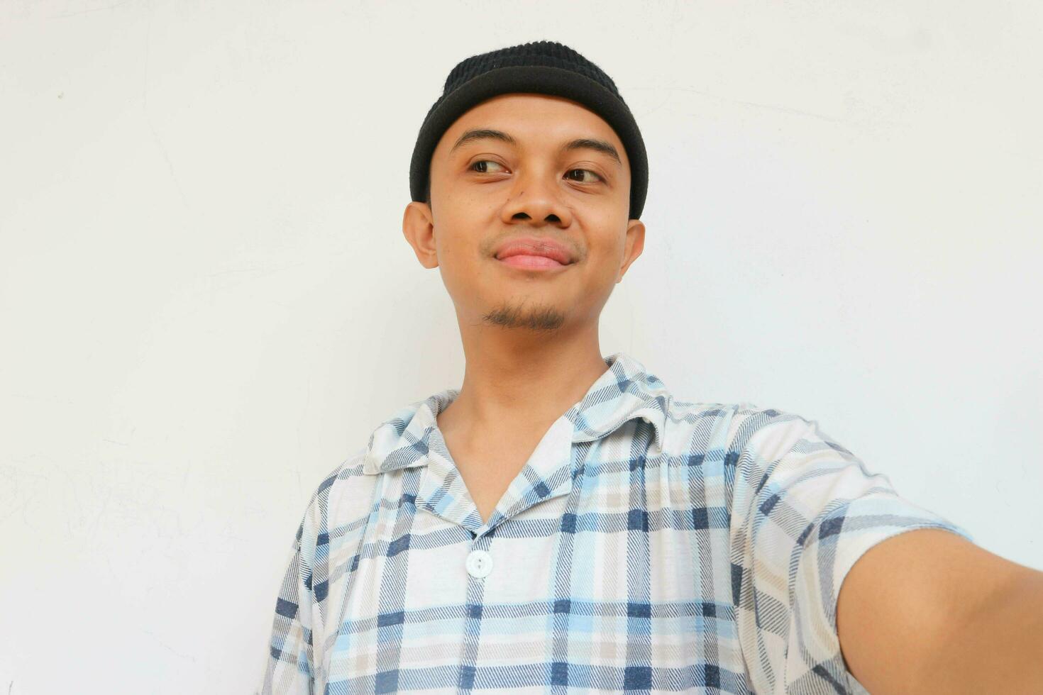 Smiling adult man wearing pajamas and beanie cap glancing to sideways to look something. Isolated on a white background photo