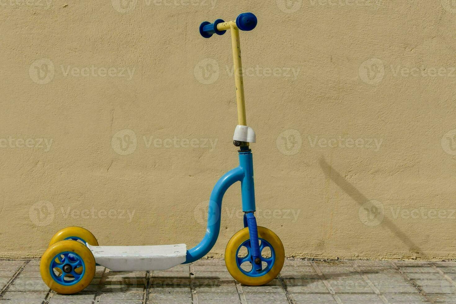 a small blue and yellow scooter sitting against a wall photo