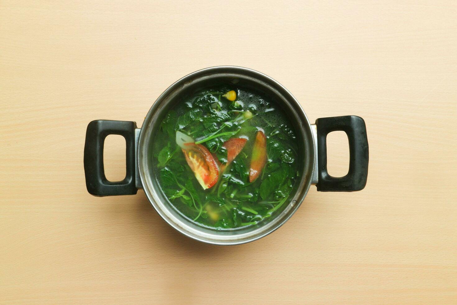 Sayur Bayam or Spinach clear soup serve in the pot isolated on wooden background photo