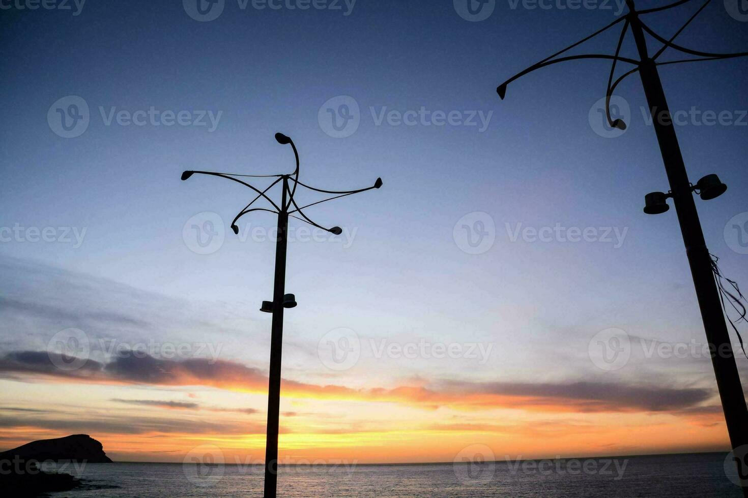 the sun sets over the ocean, and a few street lights photo