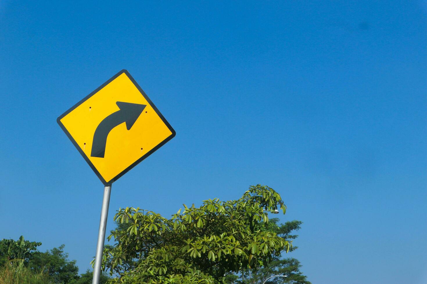 Black arrow traffic sign on yellow background on the bright sky background photo