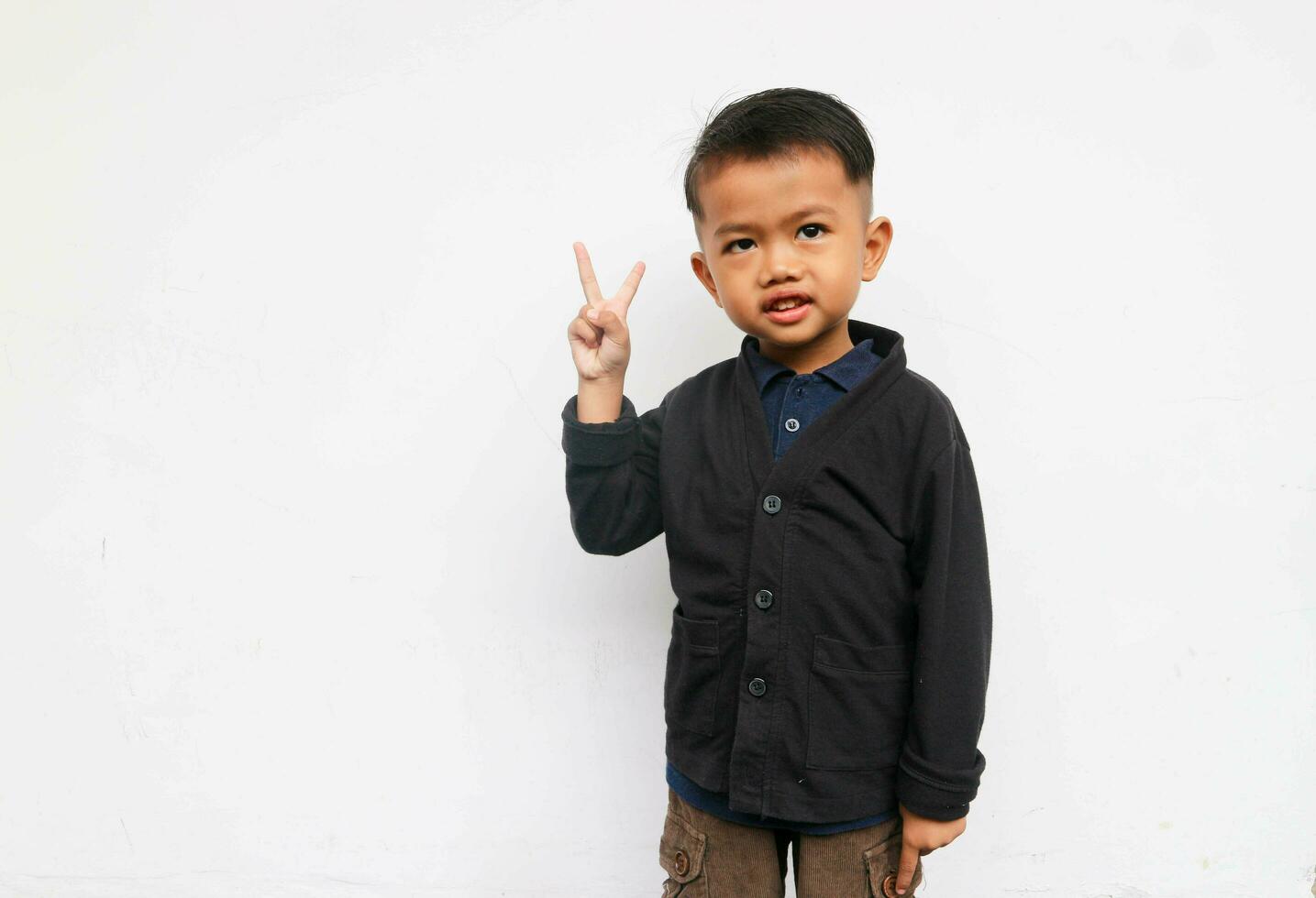 A smiling toddler boy raised hand to show V sign, isolated on white background photo