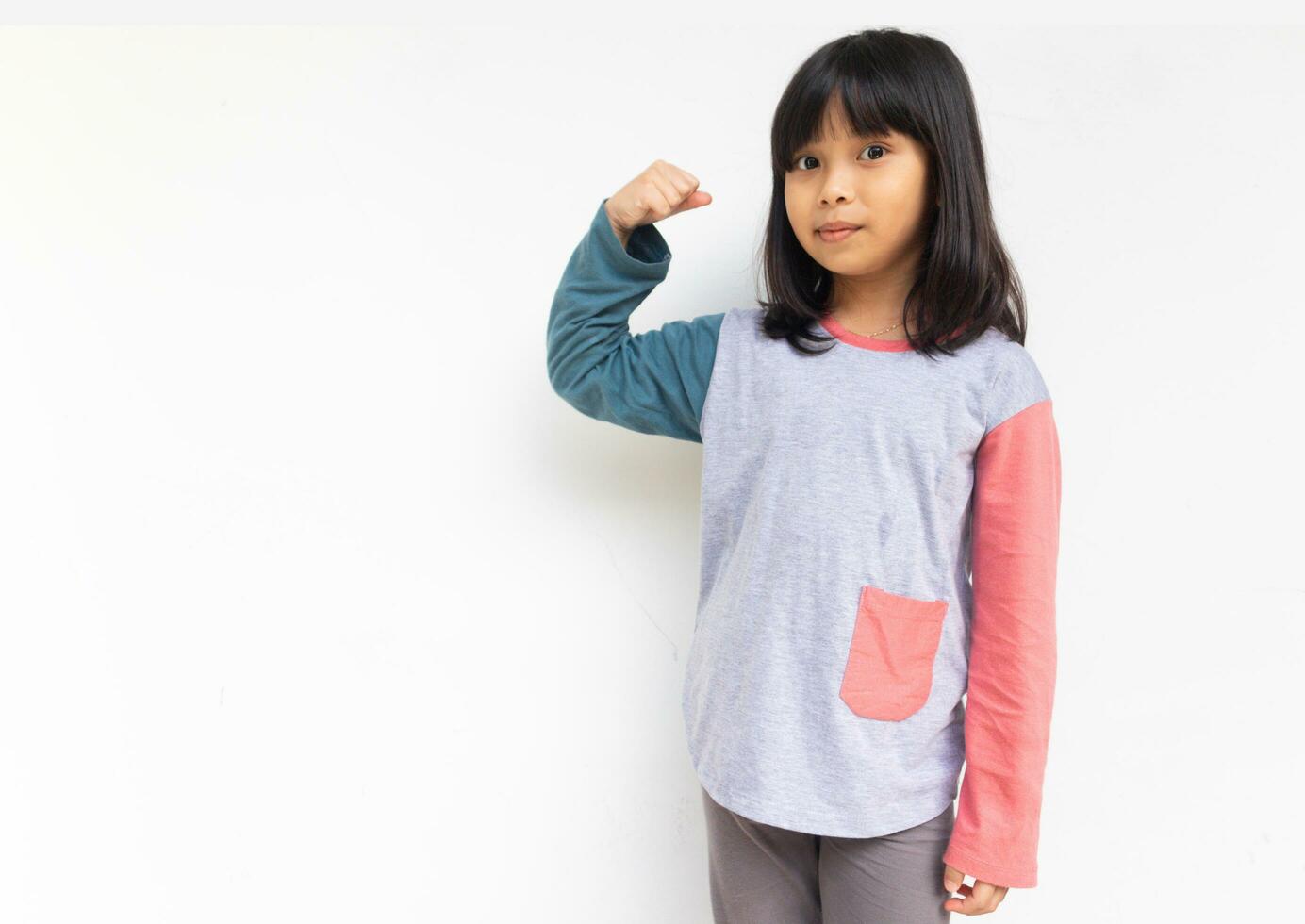 un linda confidente niña mirando a cámara elevado mano demostración su bíceps músculo foto