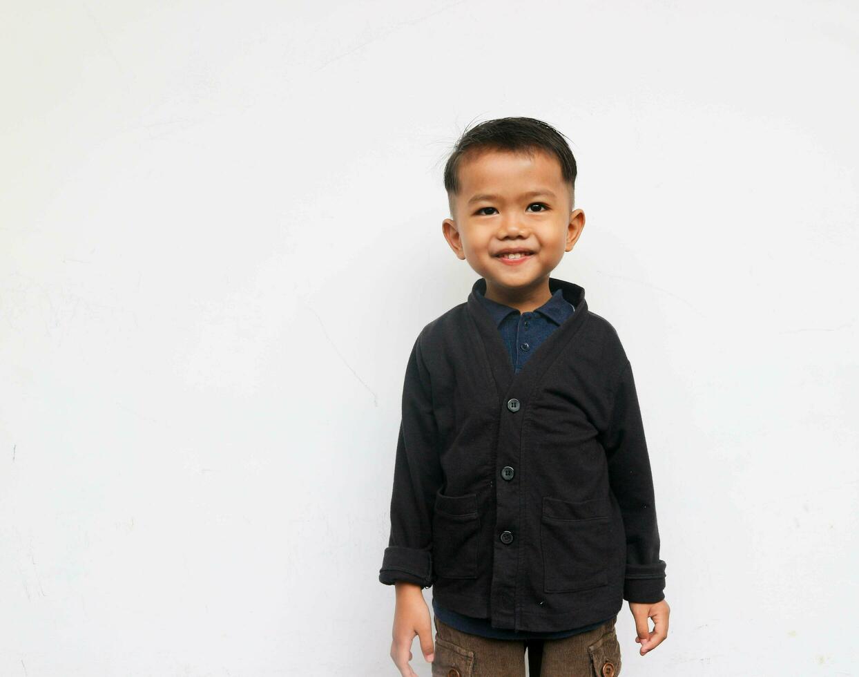 A smiling toddler boy standing while looks at the camera with confidence, isolated on white background photo