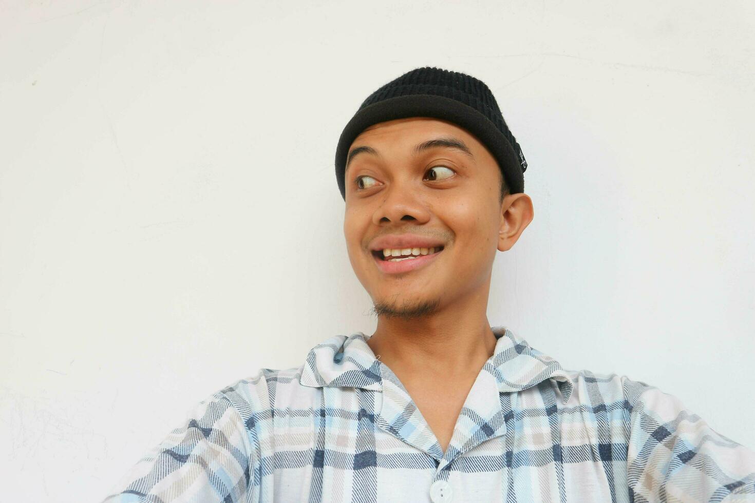 Smiling adult man wearing pajamas and beanie cap glancing to sideways to look something. Isolated on a white background photo