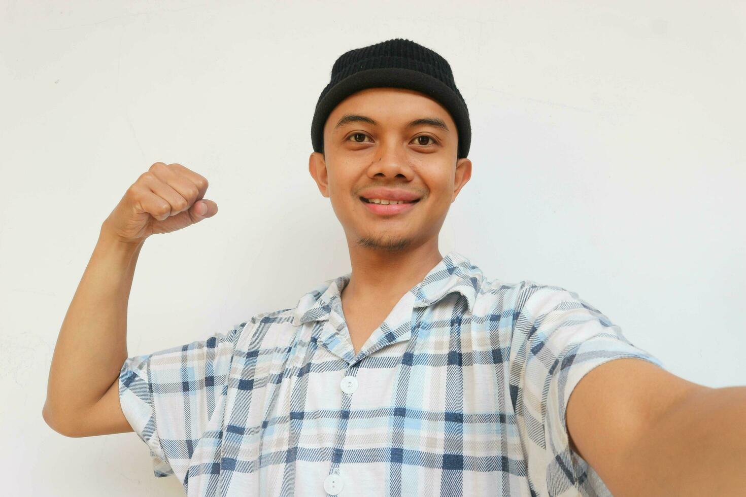 Smiling adult man wearing pajamas and beanie cap showing his bicep muscle and looking at camera. Isolated on white background photo