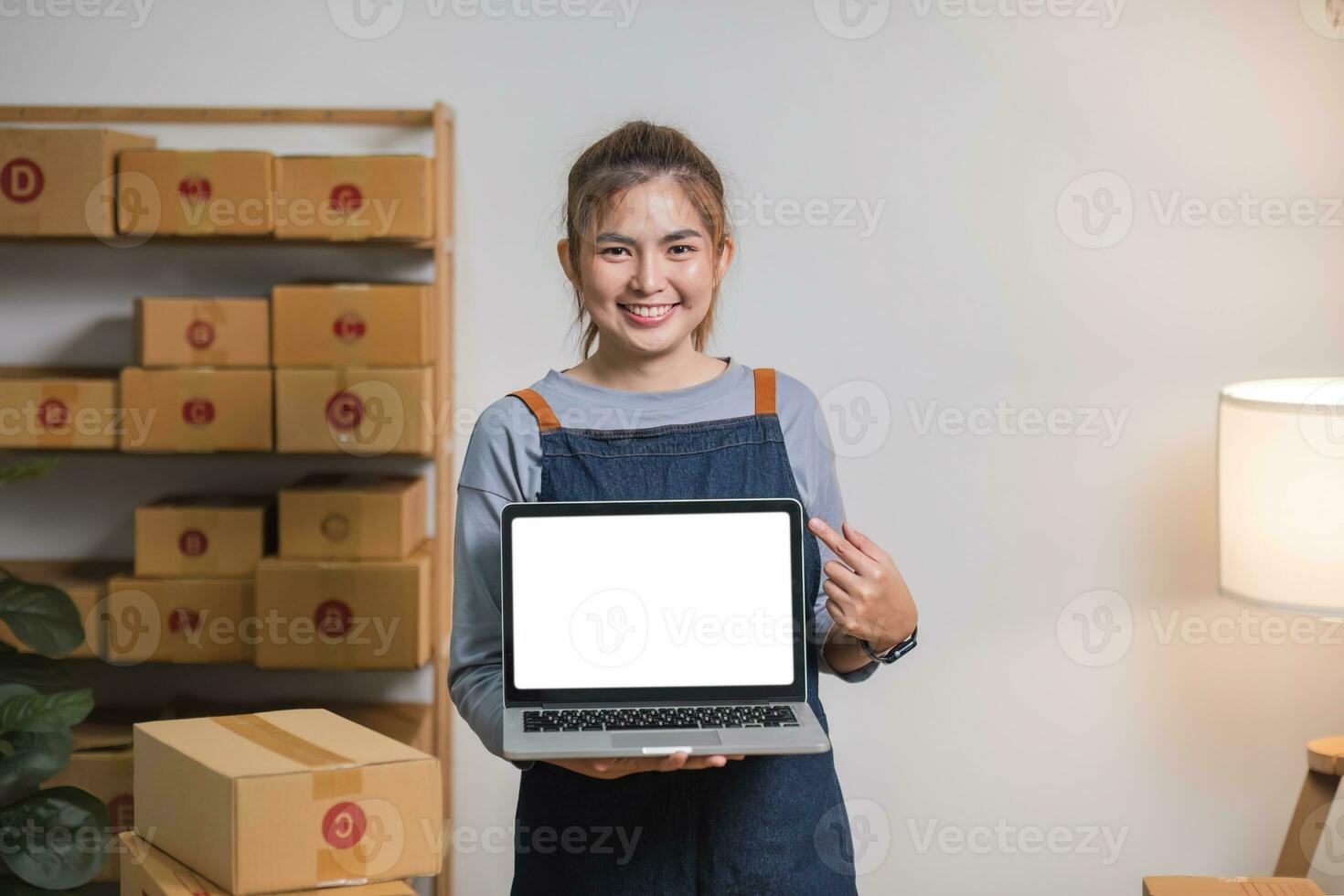 Asian SME business woman showing laptop empty screen at home office. Portrait young Asian small business owner home office, online sell marketing delivery photo