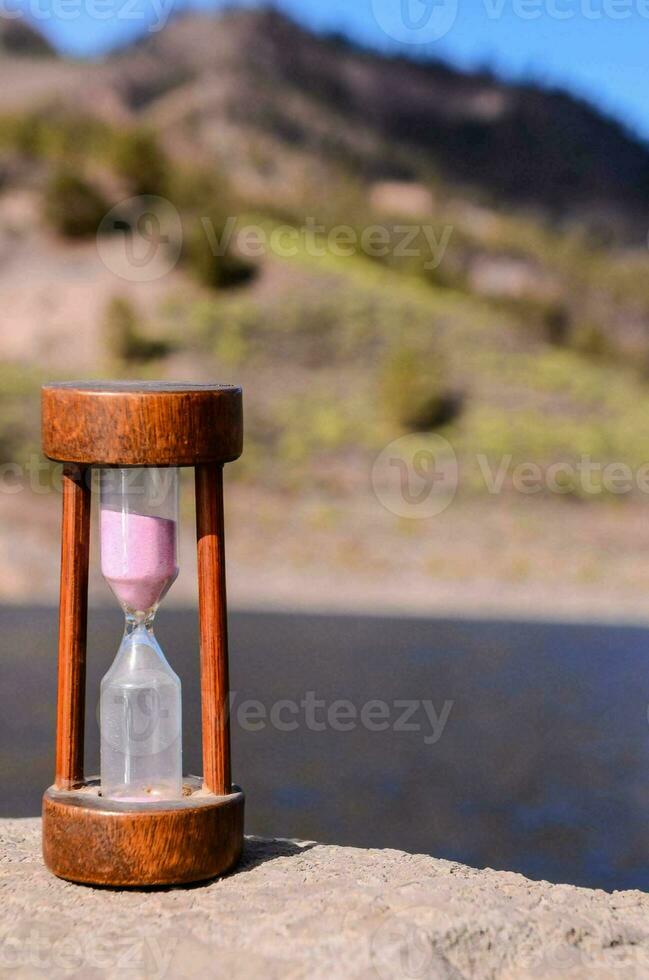 a wooden hourglass sitting on a rock near a lake photo