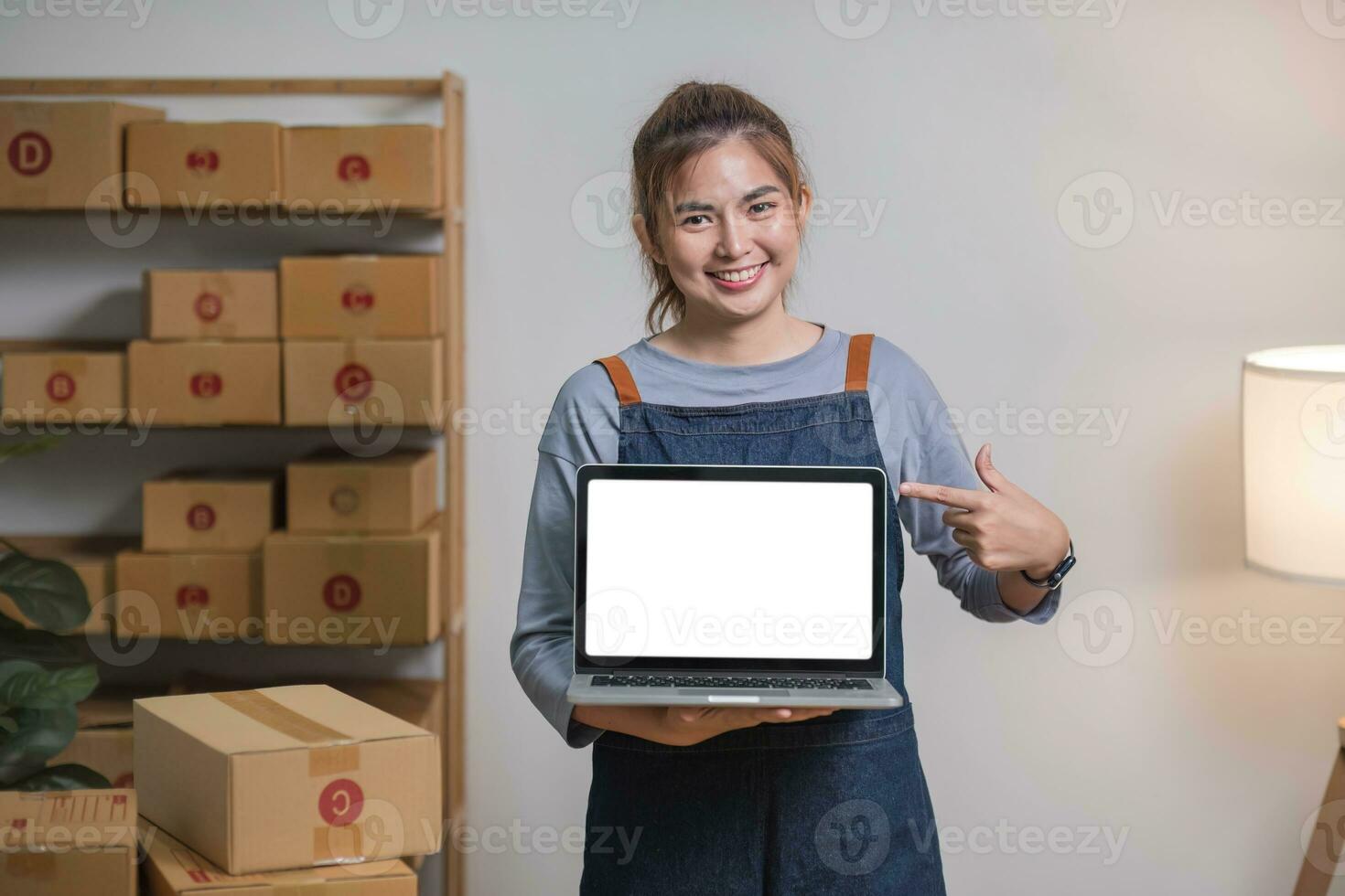 Asian SME business woman showing laptop empty screen at home office. Portrait young Asian small business owner home office, online sell marketing delivery photo