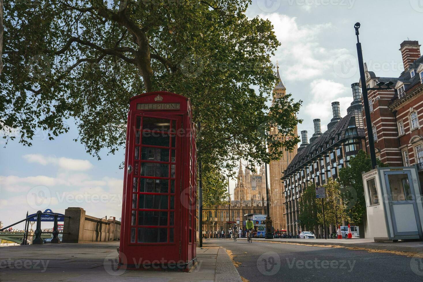 Empty red telephone booth and tree on sidewalk with famous Big Ben in background photo