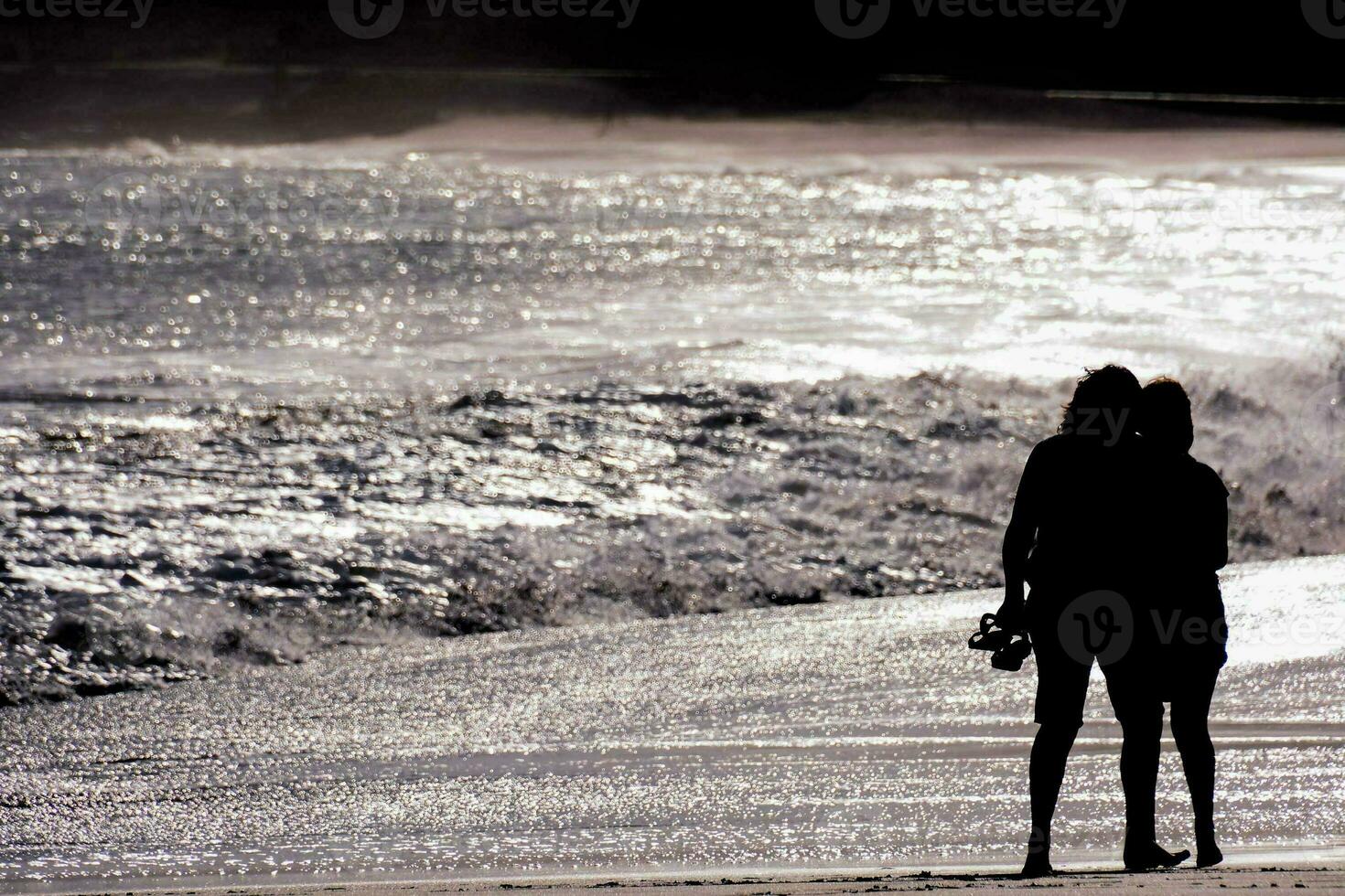 two people standing on the beach with the ocean in the background photo