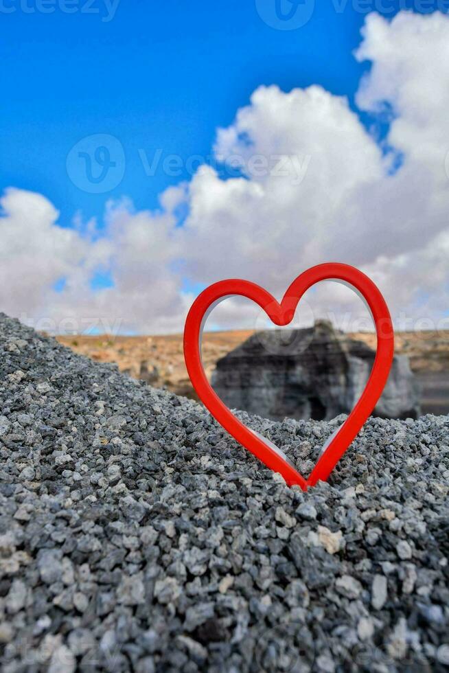 un rojo corazón conformado objeto es sentado en un grava la carretera foto