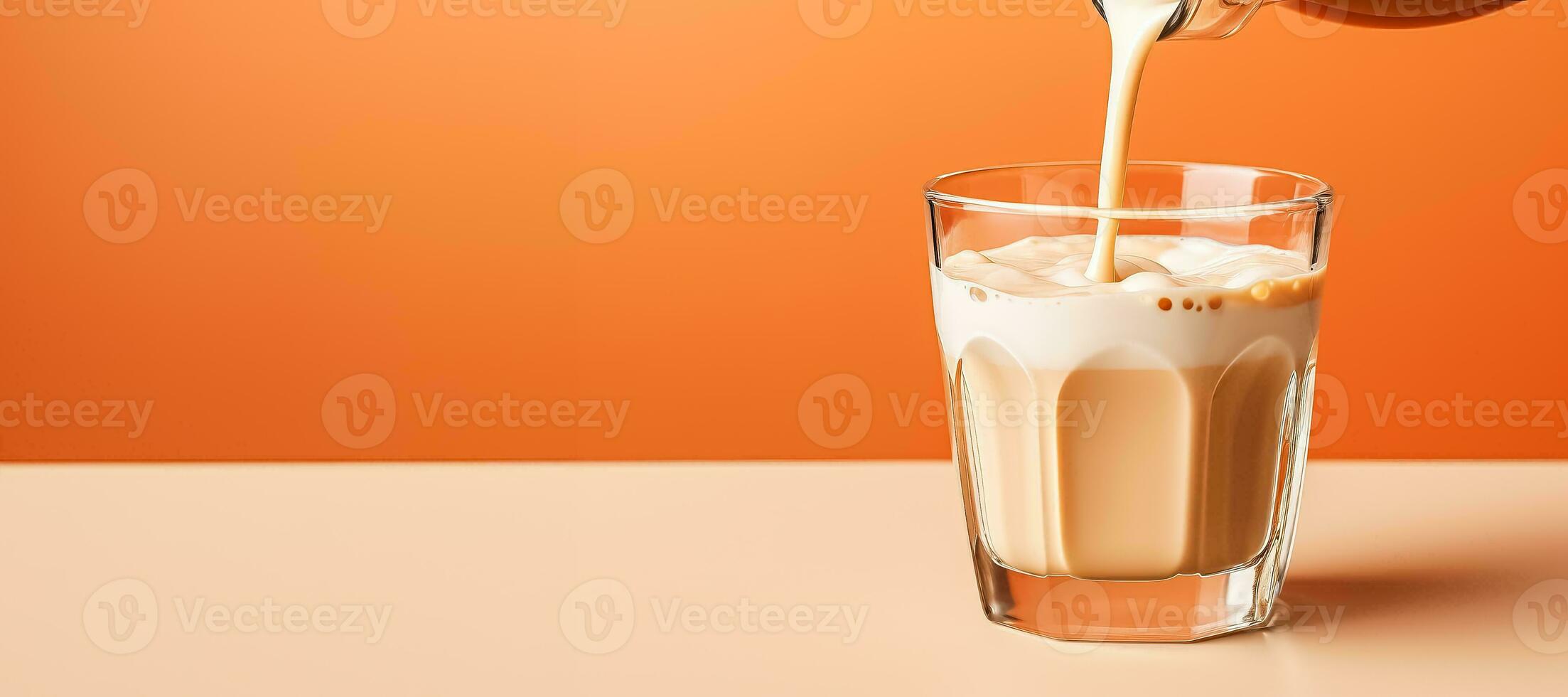 Pouring milk into glass of coffee latte isolated on pastel background with a copy space photo