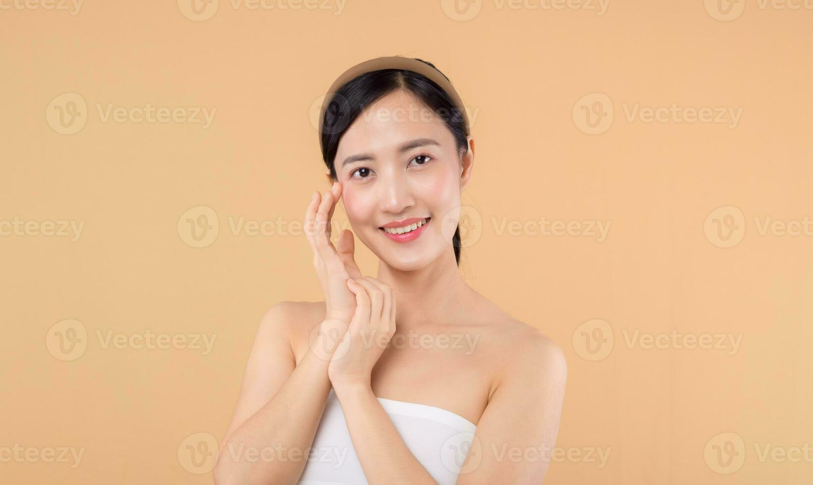 hermosa niña asiático modelo conmovedor Fresco brillante hidratado facial piel en beige antecedentes de cerca. belleza cara joven mujer con natural maquillaje y sano piel retrato. piel cuidado concepto foto