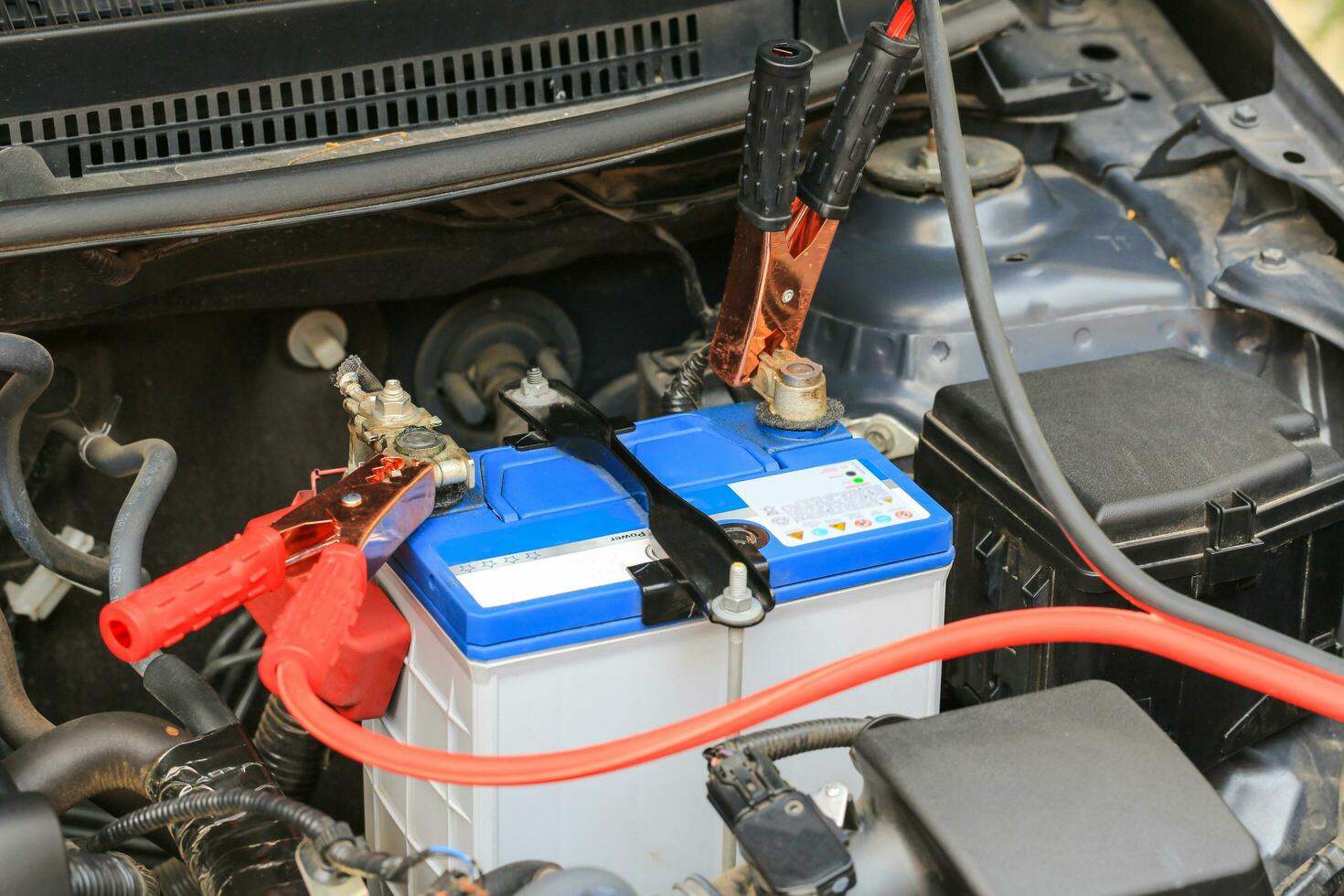 Car mechanic uses battery jumper cables charge a dead battery. photo