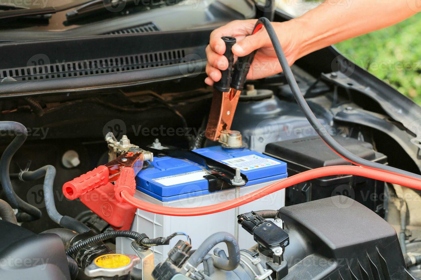 Car mechanic uses battery jumper cables charge a dead battery. photo