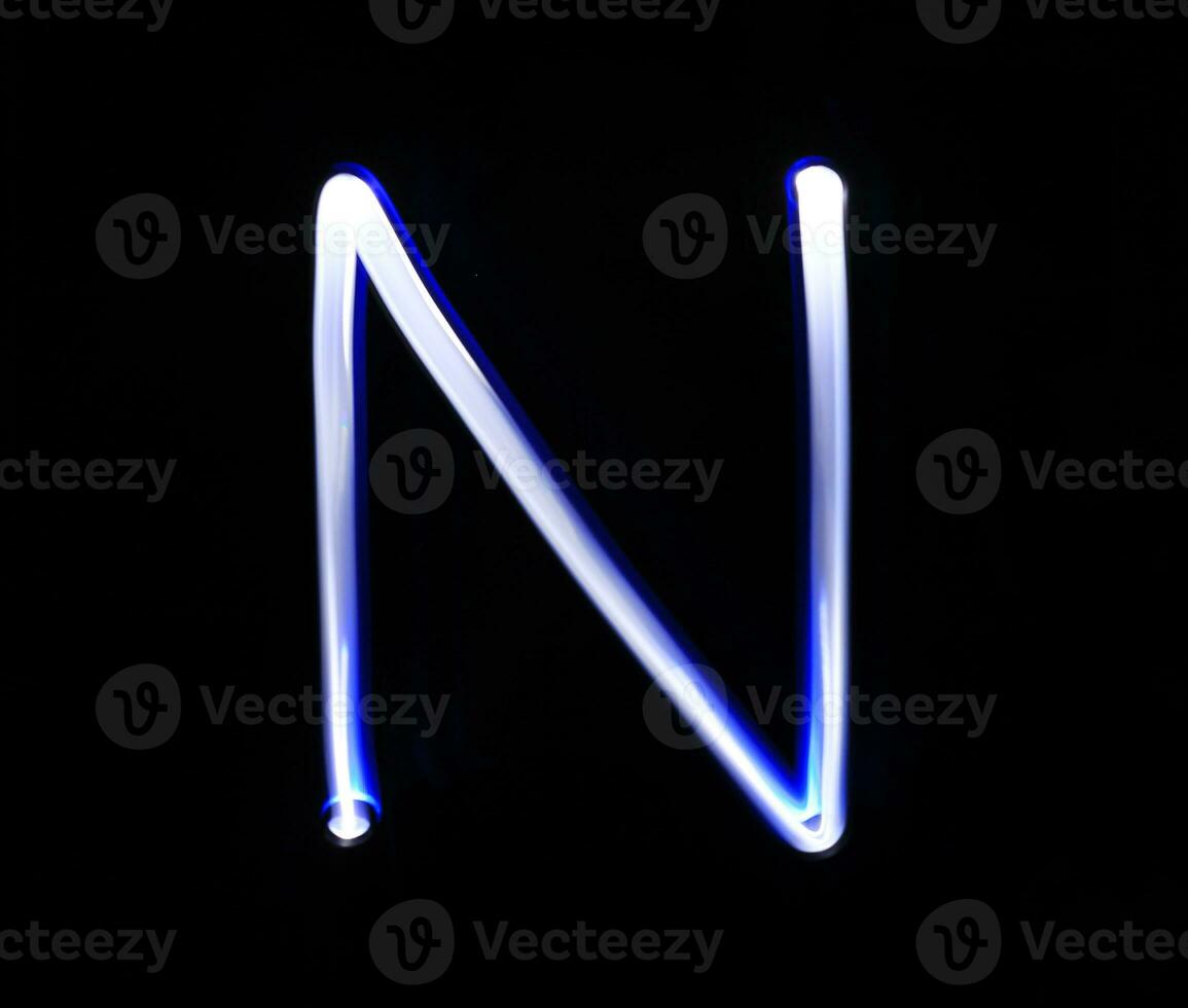 N November alphabet hand writing blue light  over black background. photo
