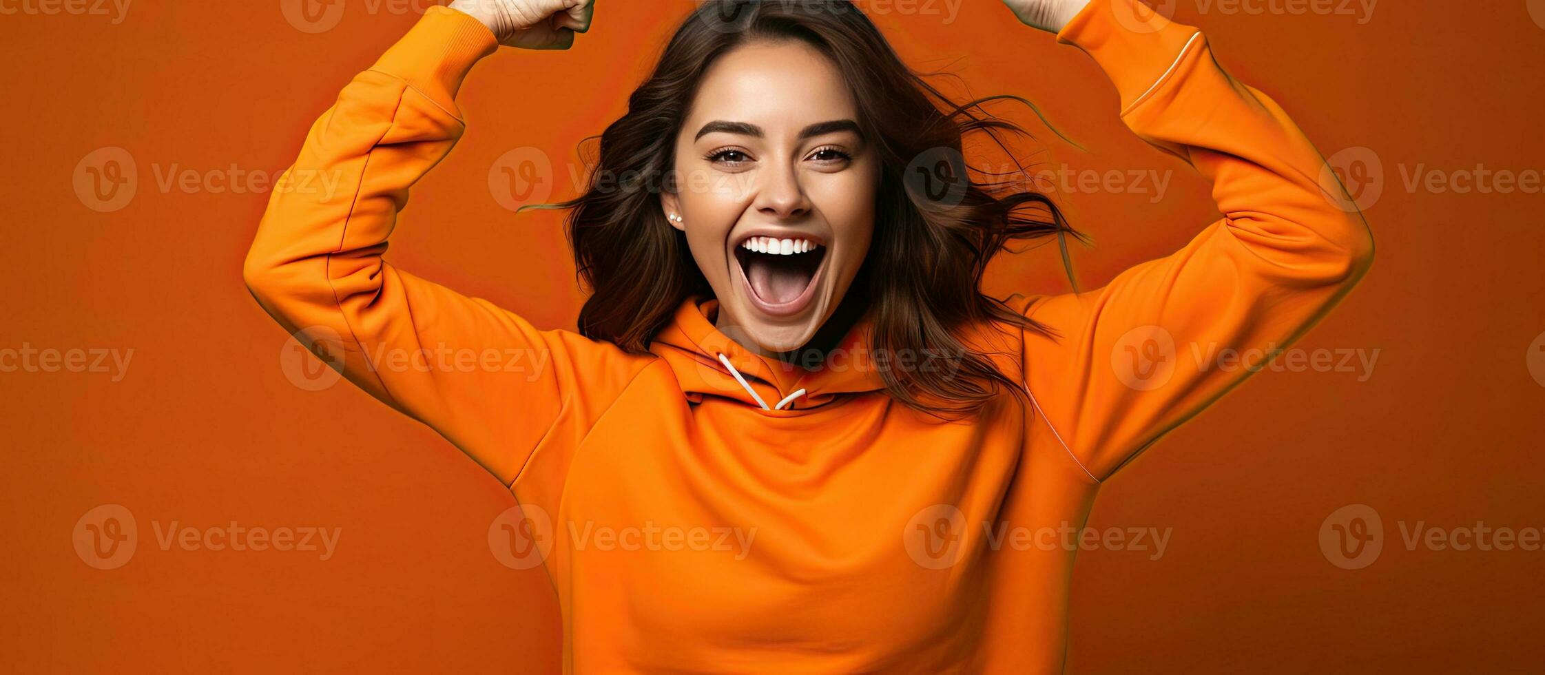 Enthusiastic young woman playfully imitates a rider dances energetically and happily points upwards dressed casually posing in a studio with an orange bac photo