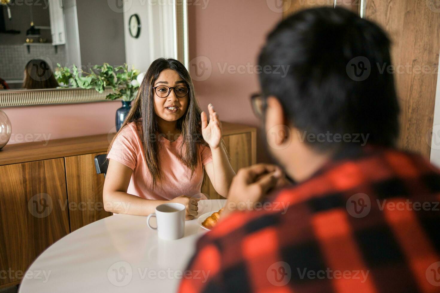 Happy indian couple having breakfast and small talk together in the kitchen - friendship, dating and family photo