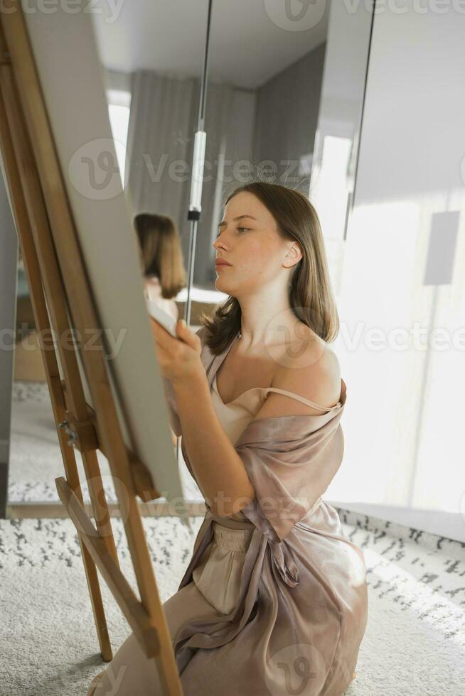 Young woman artist painting on canvas on the easel at home in bedroom - art and creativity concept photo