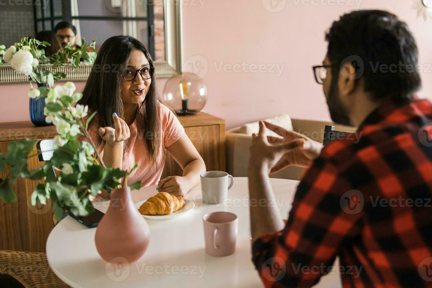 Happy couple eating breakfast and talking at dining table in morning. Indian girl and latino guy. Relationship and diversity concept photo