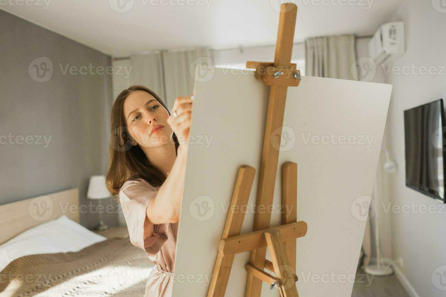 Young woman artist painting on canvas on the easel at home in bedroom - art and creativity concept photo