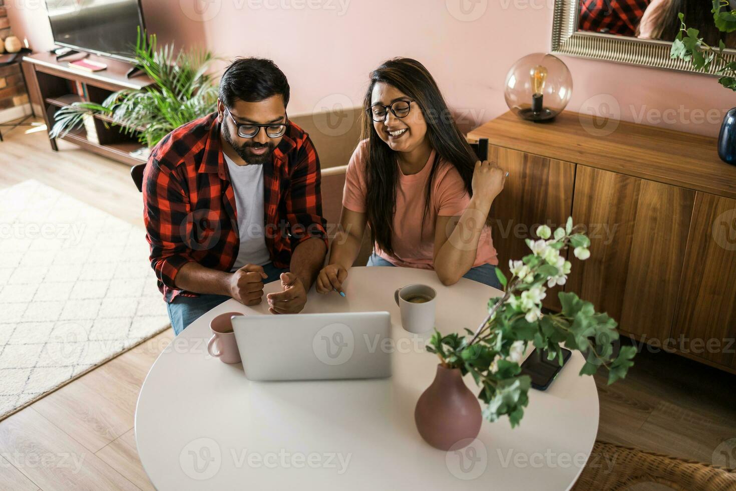 Indian family couple cuddle at desk make video call to friends using laptop webcam. Loving young spouses look at computer screen waving hands in good mood greeting parents communicating online via app photo